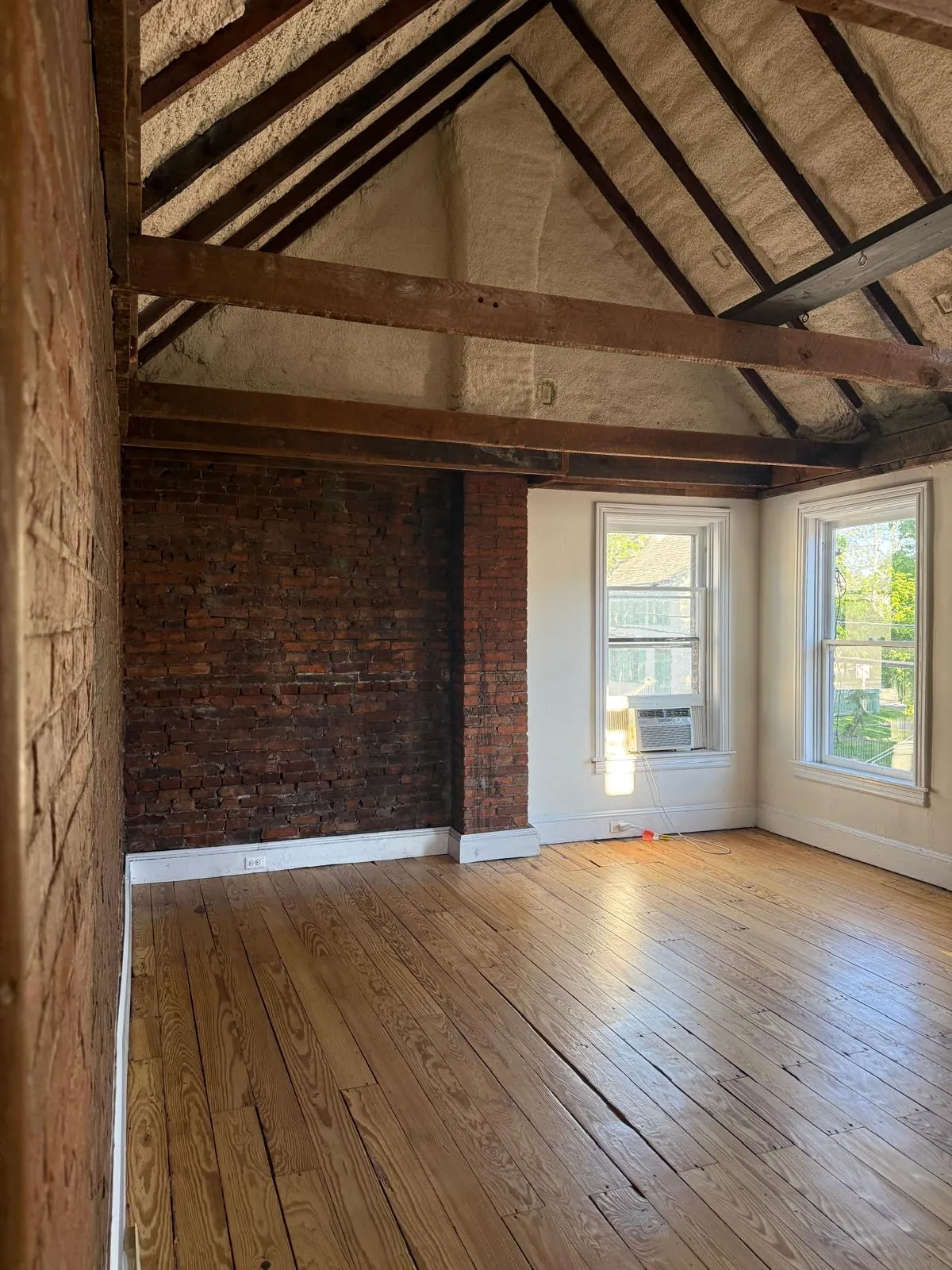 A studio room with a bare brick wall, timber beams and sunlight on the floor